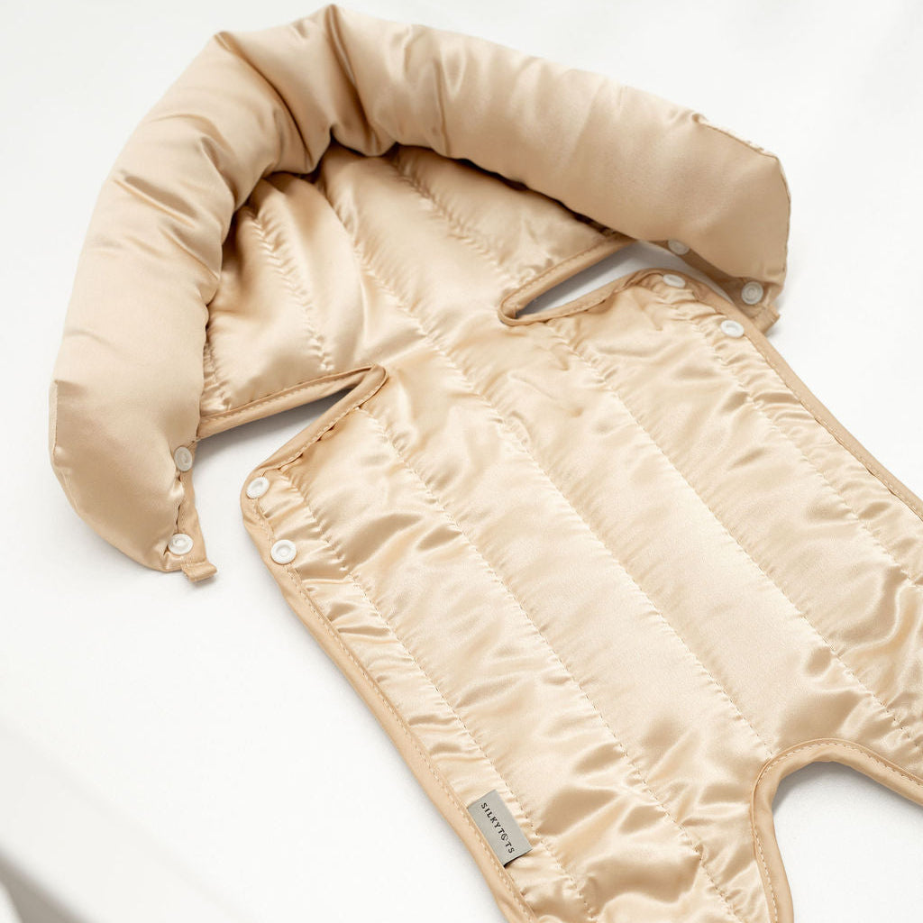 A beige padded baby blanket or quilted cover with a soft padded collar, laid flat on a white surface.